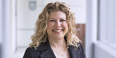Portrait of a smiling faculty member with curly hair standing in a hallway with soft natural light.